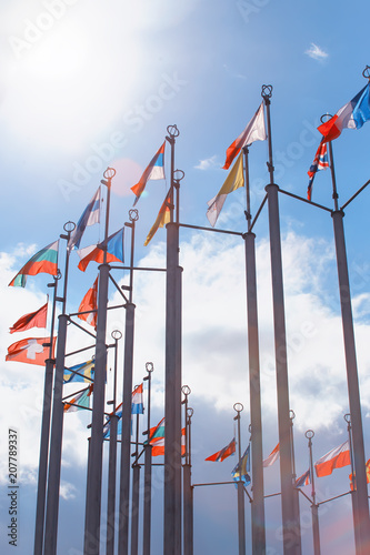 Flags of European states on flagpoles against background of cloudy sky.