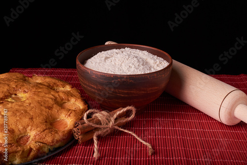 On a dark wooden table, fashionable bakeries, a bowl with flour, apricot cake and tools stand on table photo