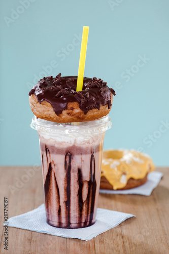 Chocolate and donuts extreme milkshakein a plastic cup on blue background. Crazy freakshake or overshake on wooden table with copy space photo