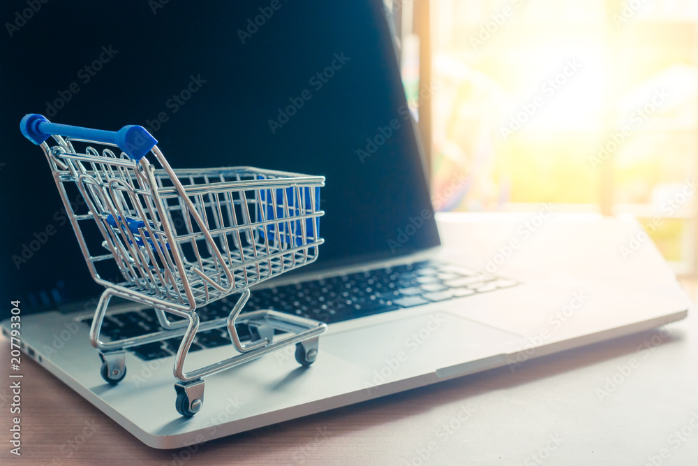 Trolley with a laptop on a wooden desk with light in background. Buy online or shopping on the web concept Trolley with a laptop on a wooden desk with light in background. Buy online or shopping on the web concept