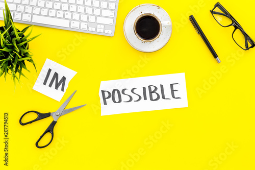From impossible to possible. Do difficult task at work concept. Cutting the part im of written word impossible by sciccors. Office desk. Yellow background top view copy space