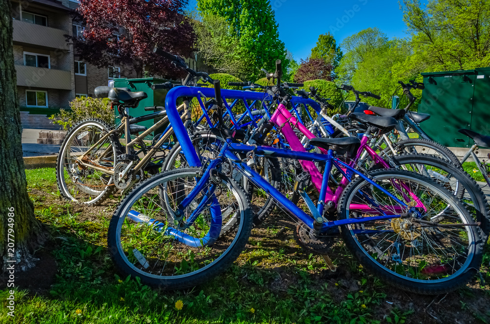 Left side view of crowded blue bike rack with dropped and deserted biycycles Left side view of crowded blue bike rack with dropped and deserted biycycles