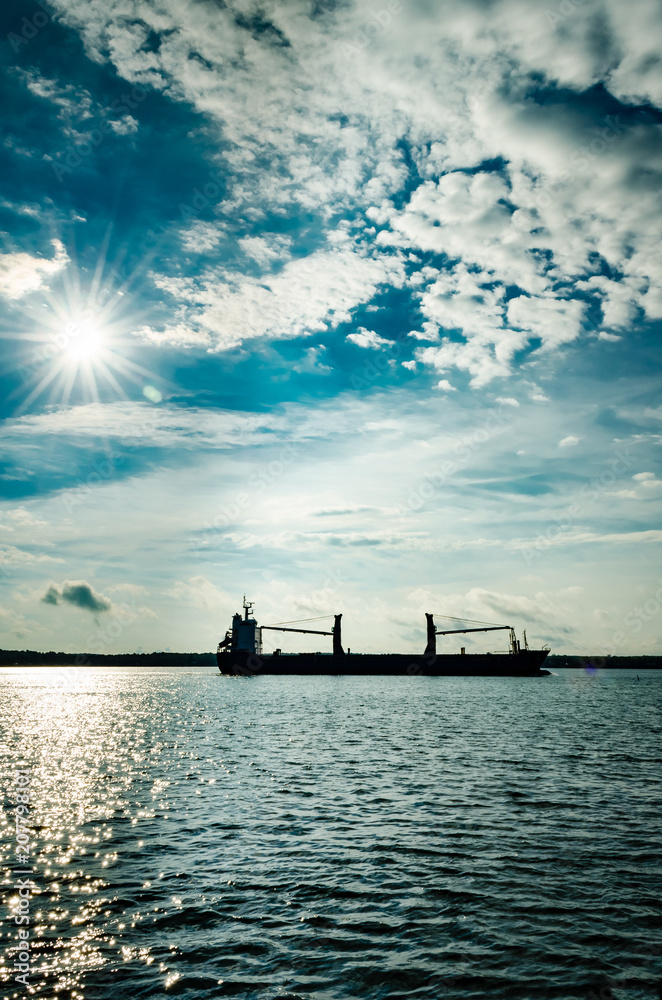 Vertical Silhouette of freight ship with sunburst