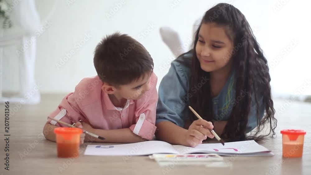 A little boy and a little girl paint in the album lying on the floor and kiss A little boy and a little girl paint in the album lying on the floor and kiss