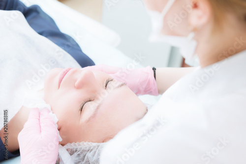 A close-up of the cleaning procedure in the office of cosmetology. The hands of the cosmetologist in pink gloves are removed from the face of a young girl with a sponge cleansing the mask