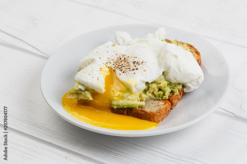 Toast and poached egg with avocado on a plate on white wooden table Toast and poached egg with avocado on a plate on white wooden table