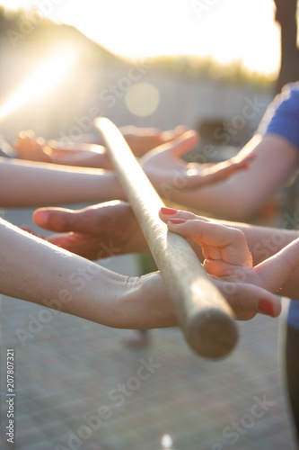 Blurred hands hold a blurred, wooden stick. teambuilding activity with a stick and hands. colleagues. rays of the sun fall, light up your hands and stick, show the way photo