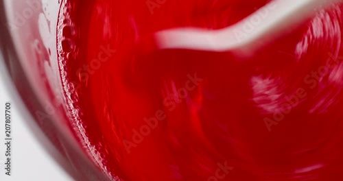 Video of stirring strawberry flavor gelatin in a bowl of water with a white plastic spoon.