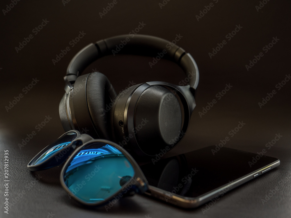 digital native Smartphone and Headphones on dark leather surface with sunglasses
