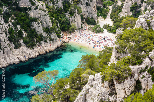 View from above of the calanque of En-Vau, a hard-to-reach narrow natural creek with white sandy beach close to Marseille and Cassis, with people sunbathing and swimming in the crystal clear water.