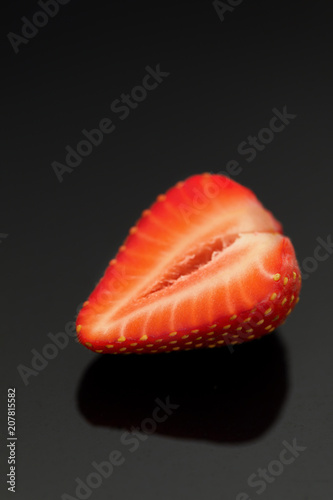 Halve of a strawberry on a reflective black background.