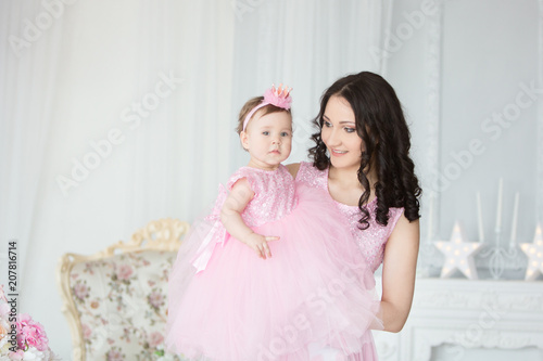 happy mother and one-year-old child girl in pink dresses on birthday party.