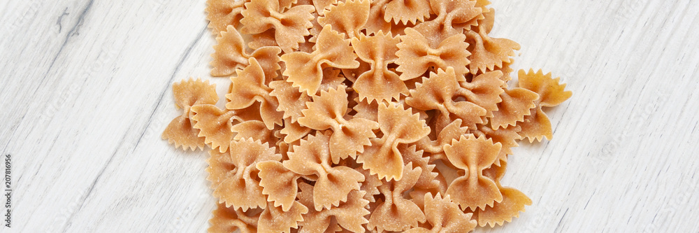 Panoramic view on spilled uncooked farfalle on a white wooden table Panoramic view on spilled uncooked farfalle on a white wooden table