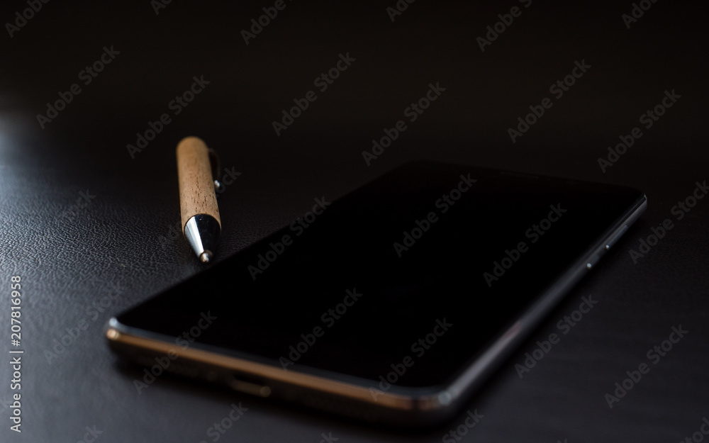 smartphone with pen on dark leather surface