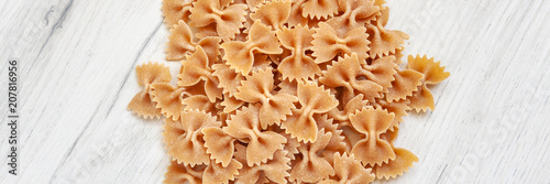 Panoramic view on spilled uncooked farfalle on a white wooden table