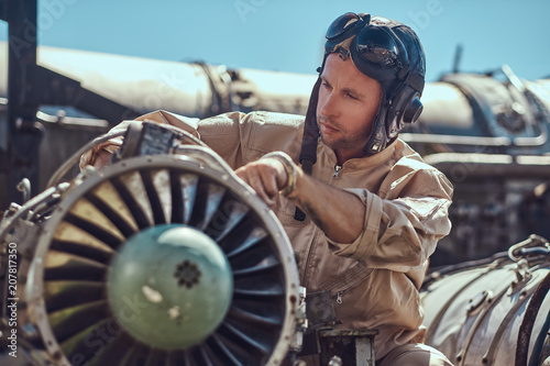 Fotografi Portrait of a mechanic in uniform and flying helmet, repairing the dismantled airplane turbine in an open-air museum