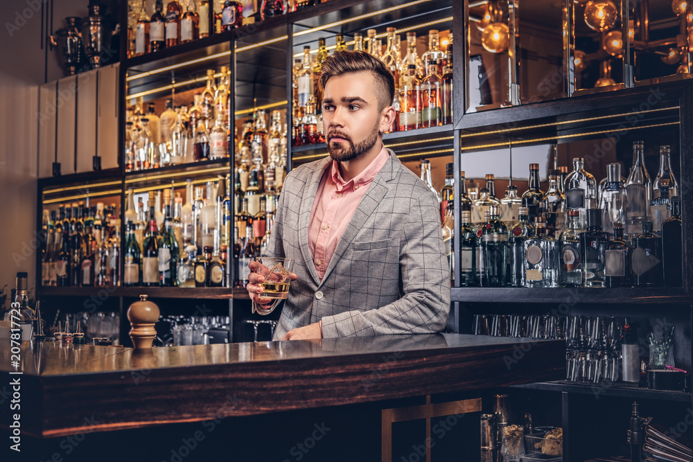 Stylish handsome male in an elegant suit holds a glass of whiskey at ...