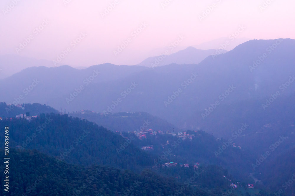 Blue hills with trees on them fading into the distance and the pink glowing sky of dusk shot in shimla. Showcases the tranquility and beauty of the place
