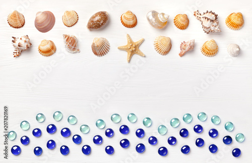 Exotic sea shells and glass beadson a white wooden background. Concept of summer travel and beach holidays. Flat lay, top view, copy space.