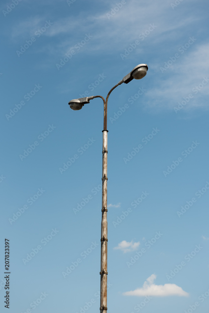 Old industrial street lamp against blue sky with white clouds. Old industrial street lamp against blue sky with white clouds.