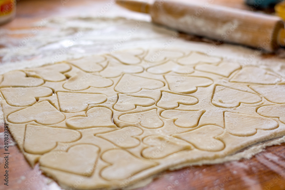 Preparation of the dough, roll out with a rolling pin and cut shapes in the form of hearts. Baking cookies for the holiday. Close-up. Preparation of the dough, roll out with a rolling pin and cut shapes in the form of hearts. Baking cookies for the holiday. Close-up.