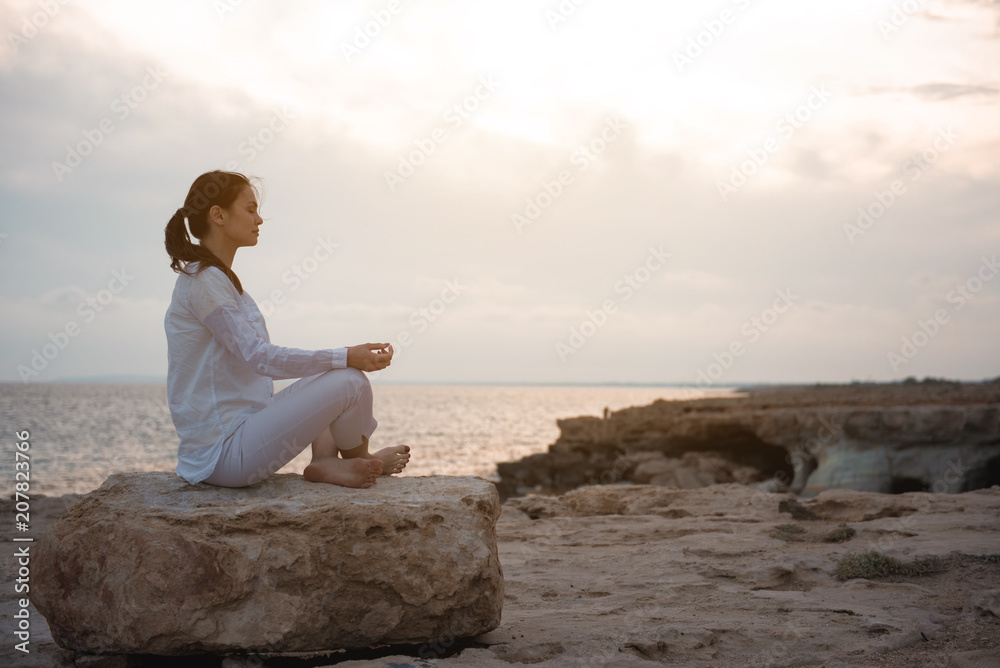 Be deep in thoughts. Full length side view of relaxed girl is sitting in lotus against beautiful ocean. She is putting elbows on knees while practicing yoga outdoors. Copy space in the right side