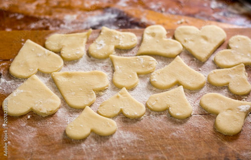 Preparation of the dough, roll out with a rolling pin and cut shapes in the form of hearts. Baking cookies for the holiday. Close-up. Preparation of the dough, roll out with a rolling pin and cut shapes in the form of hearts. Baking cookies for the holiday. Close-up.