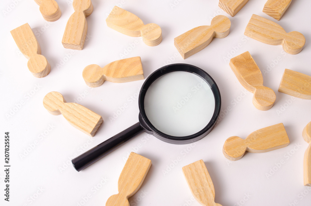 Wooden figures of people lie around a magnifying glass on a white background. Hiring for work, tracing people. The concept of the search for people and workers, human resources. Wooden figures of people lie around a magnifying glass on a white background. Hiring for work, tracing people. The concept of the search for people and workers, human resources.