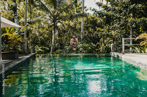 Fototapeta Naklejka Na Ścianę i Meble -  .Young and attractive tourist enjoying a morning in the pool of his hotel in Bali, Indonesia. Jumping and having fun. Lifestyle