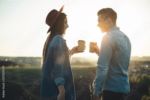 Side view of man and female drinking coffee and spending time joyfully during summer evening. They are looking at each other and smiling