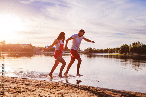 Fototapeta Naklejka Na Ścianę i Meble -  Young man and woman running on summer river bank. Couple having fun at sunset. Guys chilling