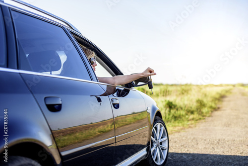 An attractive woman in a car holds a car key in her hand.