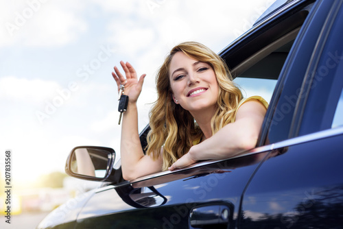 An attractive woman in a car holds a car key in her hand.