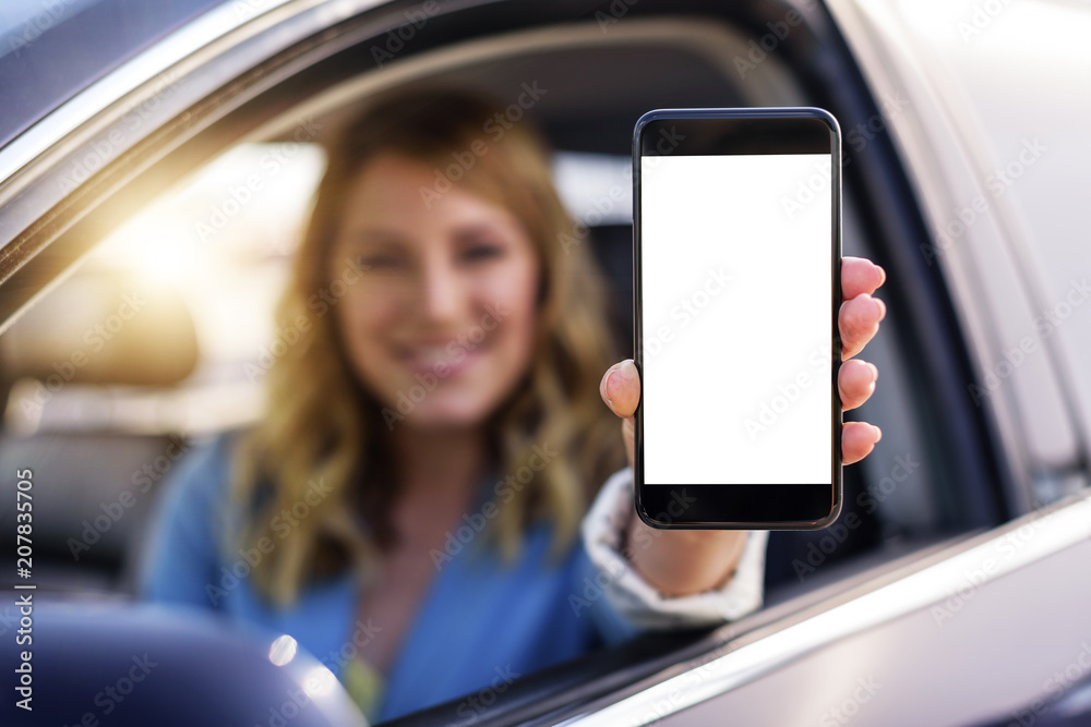 Young woman in auto shows smartphone with blank screen.