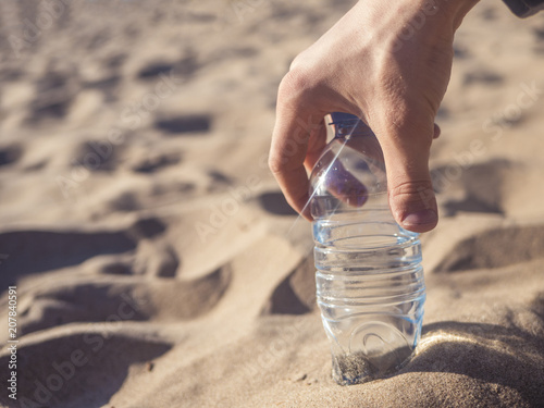 hand holding bottle with water on the sandy sea beach