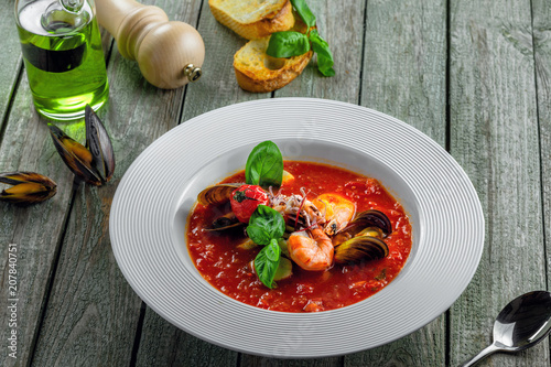 Excellent soup made of tomato and seafood on a rustic wooden table. Plate of healthy Italian meal.