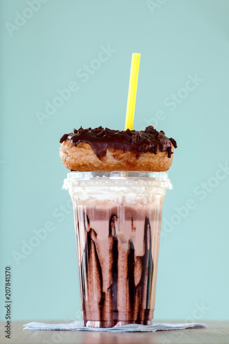 Chocolate and donuts extreme milkshakein a plastic cup on blue background. Crazy freakshake or overshake on wooden table with copy space photo