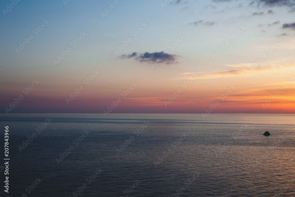 Sunset at the beach with some clouds in the sky. Blue and pink shades with dark clouds. Quiet place. Relaxing scene of beaches. Beautiful natural landscape. Peaceful view