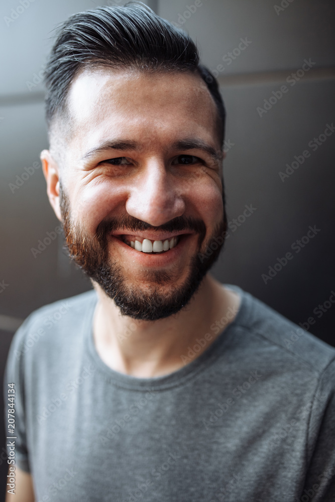 Portrait of a beautiful stylish guy, hipster dressed in a gray empty t-shirt standing on a black wall background. Empty space for logo or design. Portrait of a beautiful stylish guy, hipster dressed in a gray empty t-shirt standing on a black wall background. Empty space for logo or design.