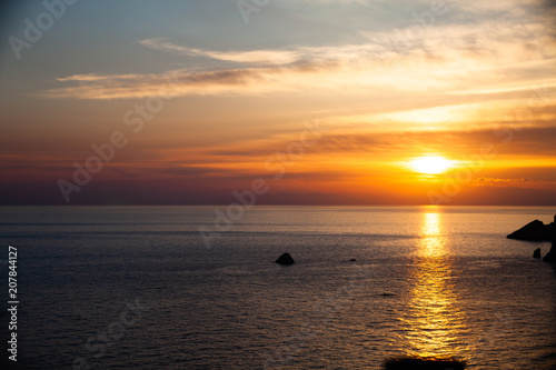 Sunset on the beach with clouds. Calm sea water. Beautiful colors in the sky. Blue and orange shades. Quiet place. Relaxing scene of beaches. Pretty natural landscape © Artur