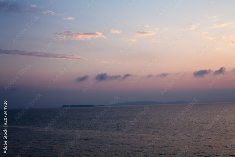 Sunset at the beach with some clouds in sky. Blue and pink shades with dark clouds. Quiet place. Relaxing scene of beaches. Beautiful natural landscape. Peaceful view