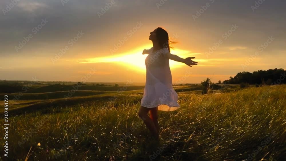 Beautiful girl wearing white dress running through beautiful field at sunset. Young woman jogging at the meadow and enjoying freedom. Summer leisure at nature concept.