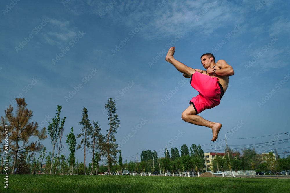 Tricking on lawn in park. Man makes kick with his foot in jump. Martial arts and parkour. Street workout. Tricking on lawn in park. Man makes kick with his foot in jump. Martial arts and parkour. Street workout.