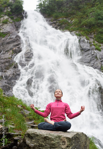 Young woman practising yoga on stone in front of beautiful Balea waterfall in Romania. Connecting with nature