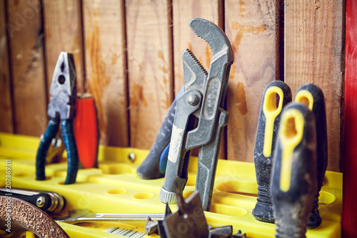 A close-up of a set of tools: pliers, a screwdriver, a wrench on a yellow stand