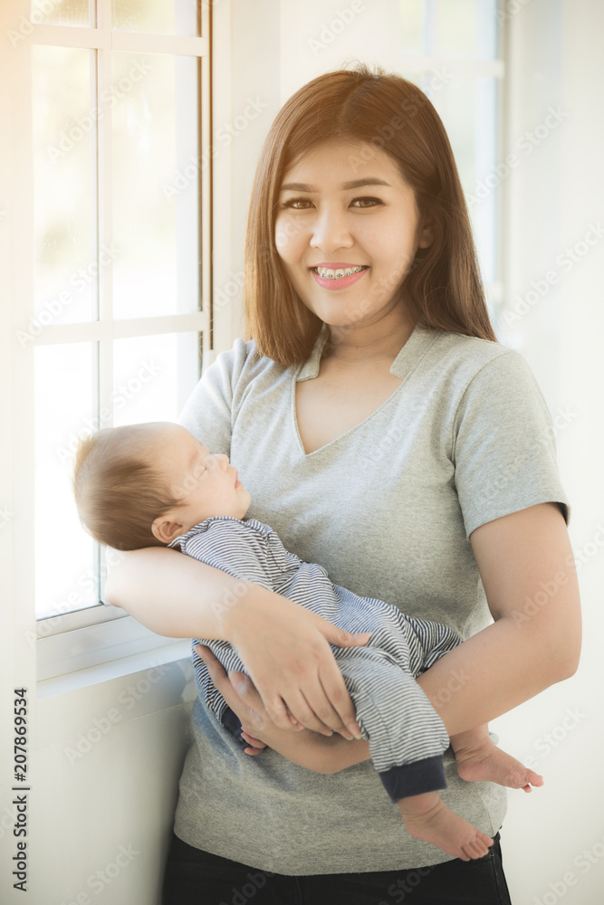Asian Mother Cuddling Baby Daughter At Home In Front Of Window Asian Mother Cuddling Baby Daughter At Home In Front Of Window