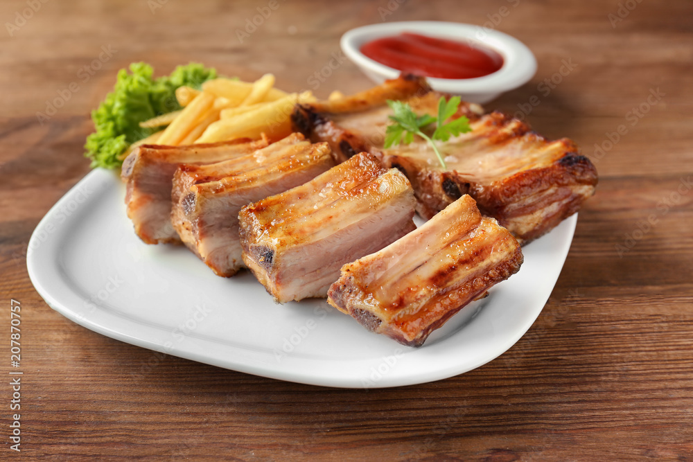 Plate with delicious grilled ribs on wooden table