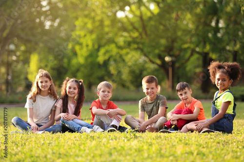 Cute little children sitting on grass outdoors on sunny day