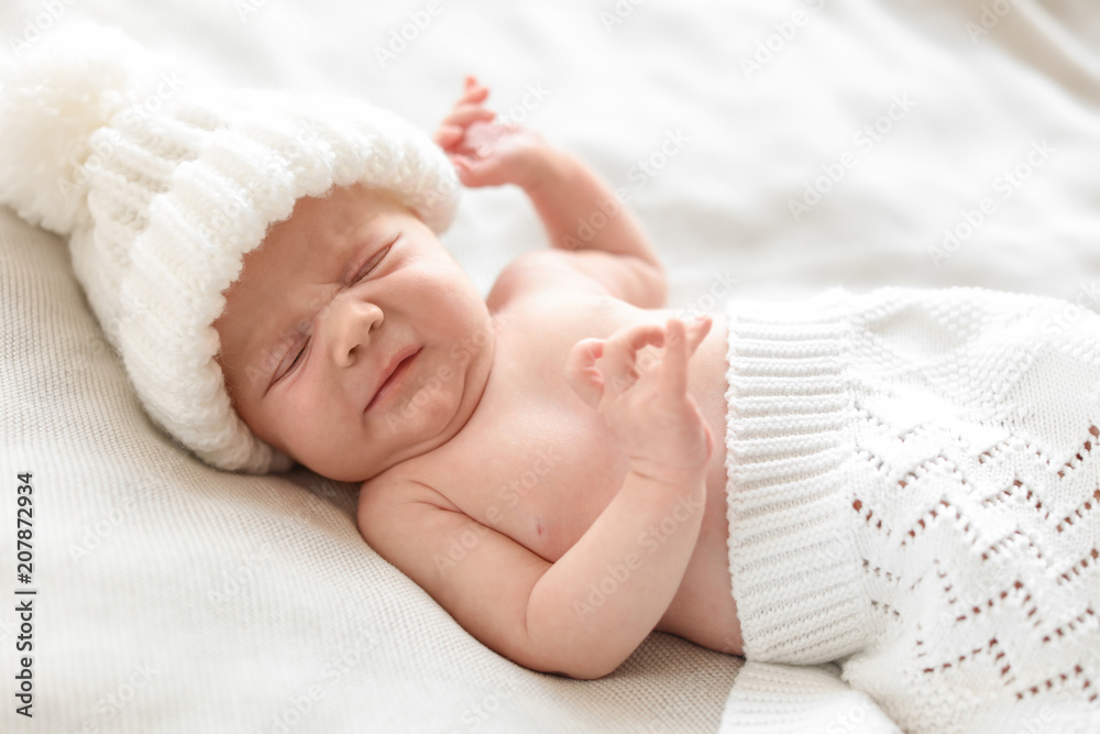 Adorable newborn baby in warm hat lying on bed