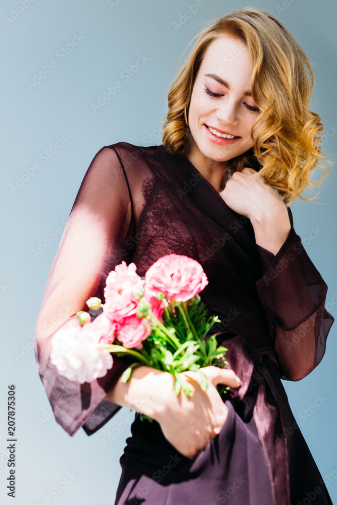 low angle view of beautiful smiling girl holding pink flowers isolated on grey low angle view of beautiful smiling girl holding pink flowers isolated on grey